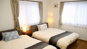 Et hotelværelse med to enkeltsenge, trægavle, et natbord med lampe og gardiner ved vinduerne.