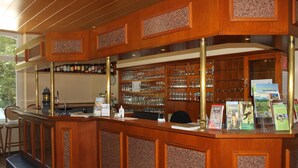 A wooden bar area with shelves of glassware and a counter with a menu. - Hotel Bergische Schweiz (Velbert)