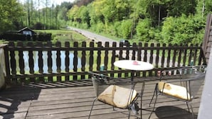 A wooden deck with a metal table and two chairs, a white tablecloth, and a metal fence. - Hotel Bergische Schweiz (Velbert)