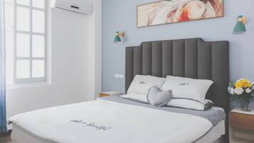 A neatly arranged bedroom with a bed, bedside tables, a wall-mounted air conditioner, a window, and a painting.