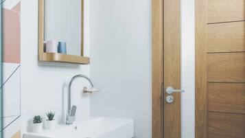 A modern bathroom with a white sink, a mirror with a gold frame, and a wooden door.
