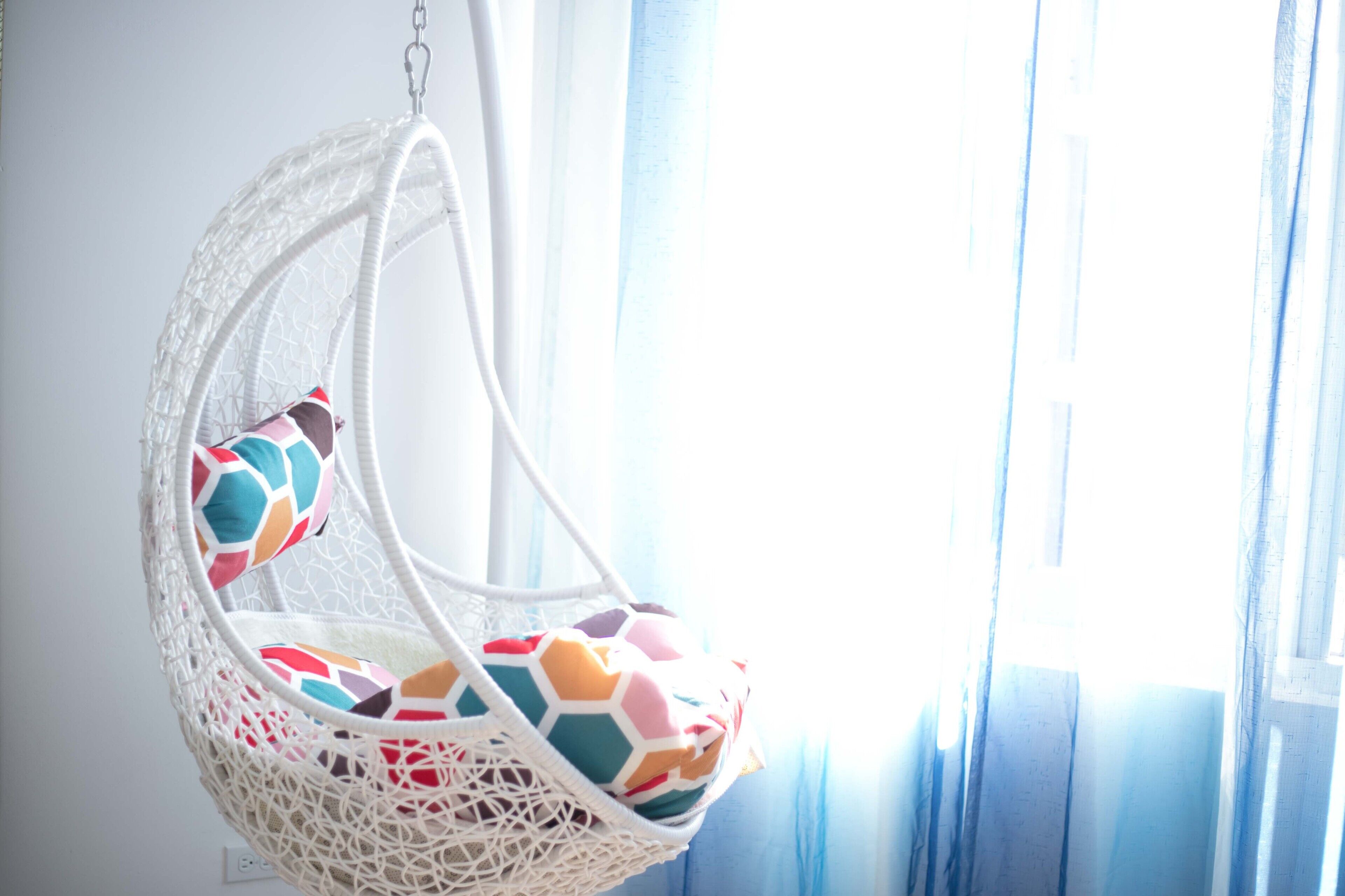 A white hanging chair with a colorful cushion.