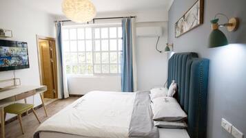 A bedroom with a bed, a desk, a chair, a television, and a window with curtains.