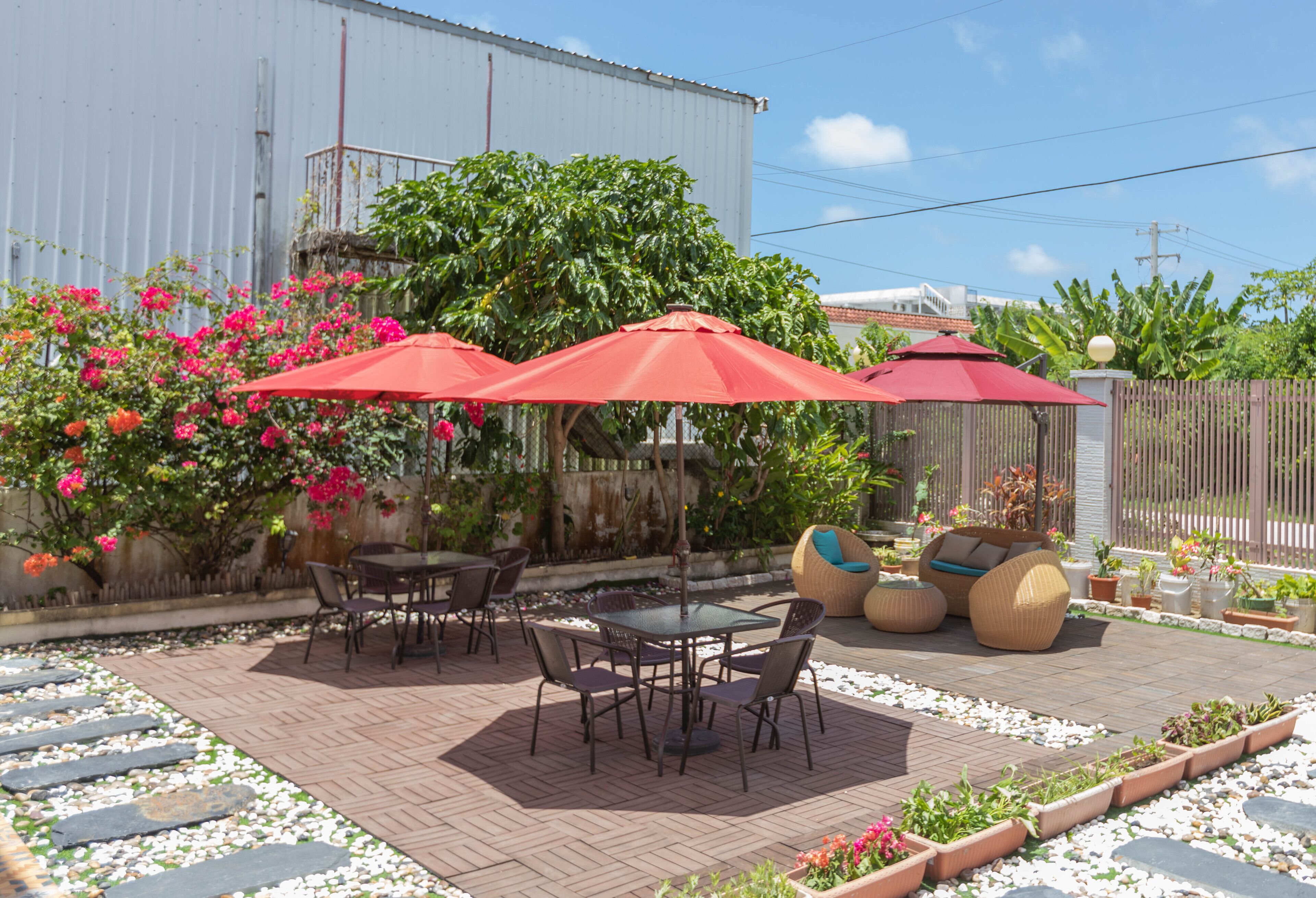 An outdoor patio with a brick floor, surrounded by potted plants and a wooden fence.