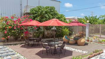 An outdoor patio with a brick floor, surrounded by potted plants and a wooden fence.