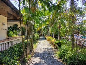 Un chemin pavé, bordé d’une végétation luxuriante et de palmiers, mène à un bâtiment doté d’un balcon.