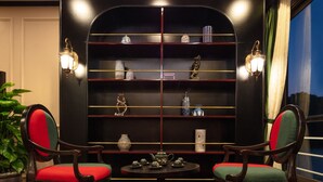 A room with a dark wooden bookshelf, two chairs with red and green cushions, and a small round table with teapots. - Orchid Premium Cruises (Hai Phong)