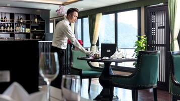 A restaurant with a bar area, green upholstered chairs, and a view of mountains through large windows.