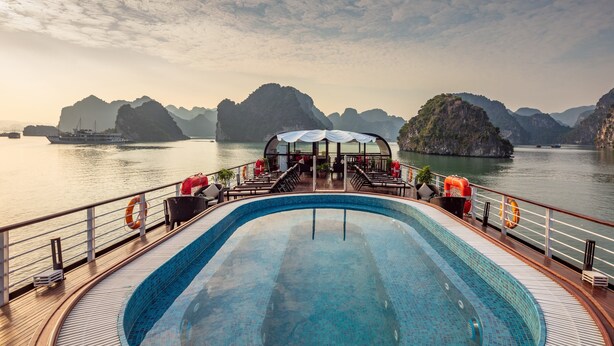 A pool area with a view of the sea and distant islands, deck chairs, and a covered seating area. - Orchid Premium Cruises (Hai Phong)