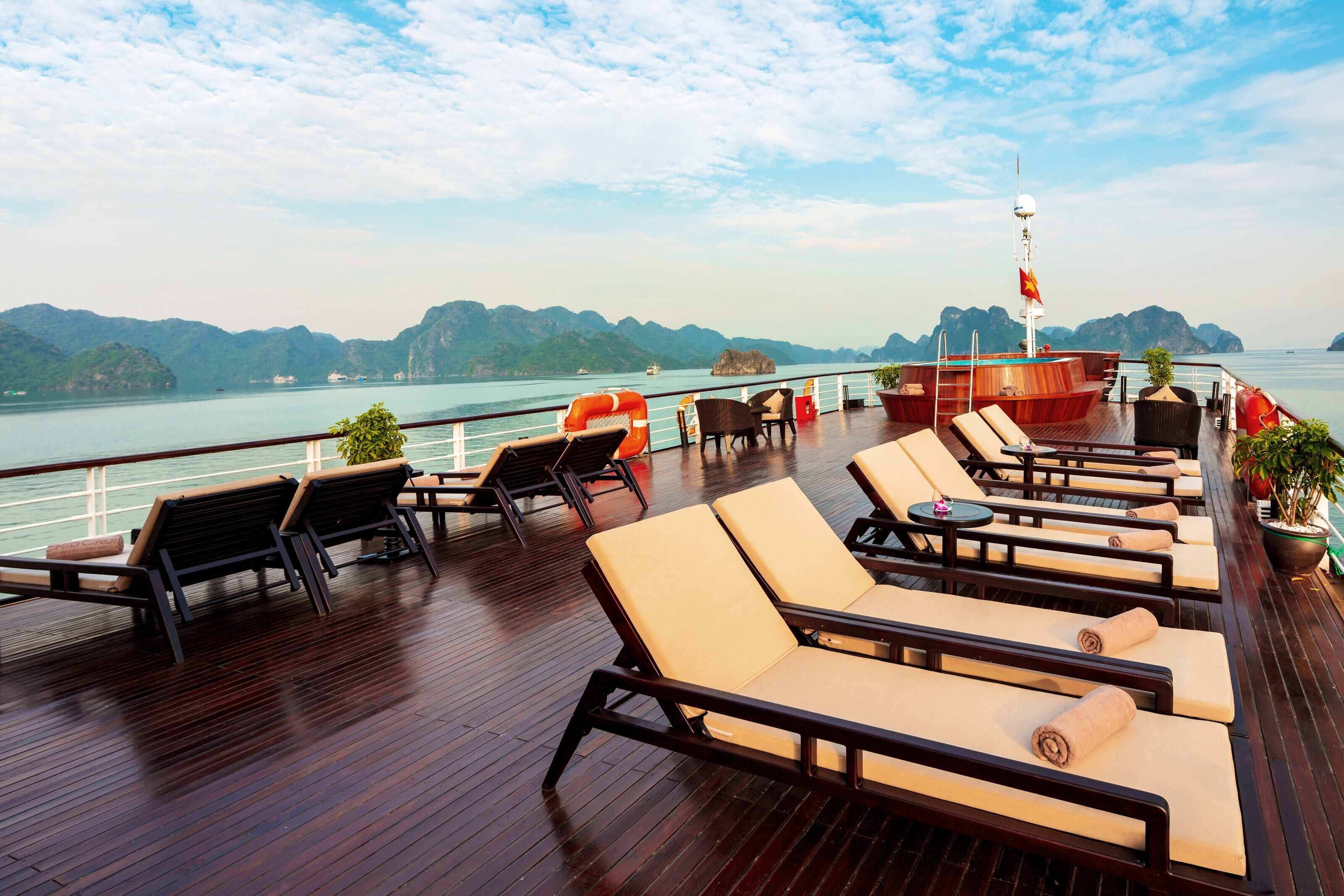 A deck with lounge chairs and tables, a flag, and a view of the water and mountains.