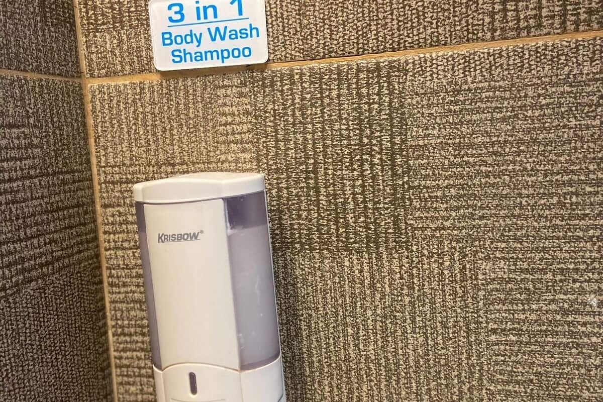 Yhdistetty suihkugeeli-, shampoo- ja saippua-annostelija, joka on kiinnitetty kuvioituun seinään.