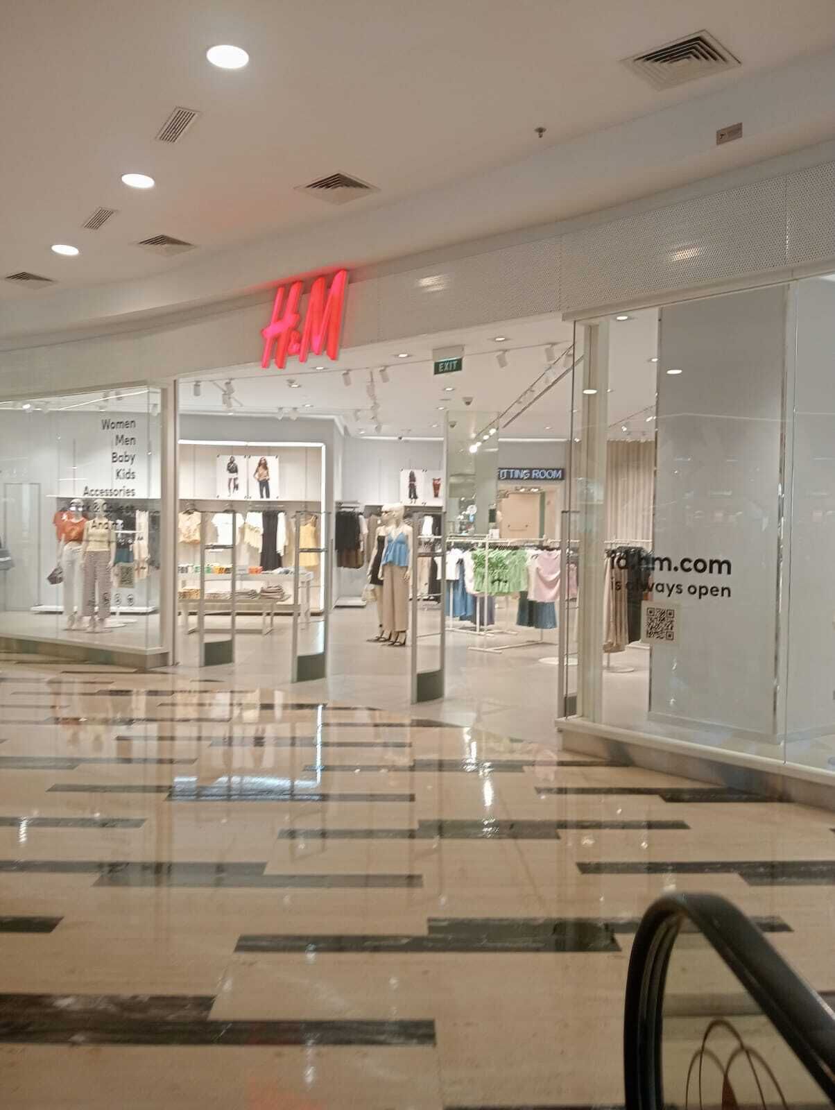 Interior de un centro comercial con una tienda H&M, escaparates de vidrio y piso pulido.