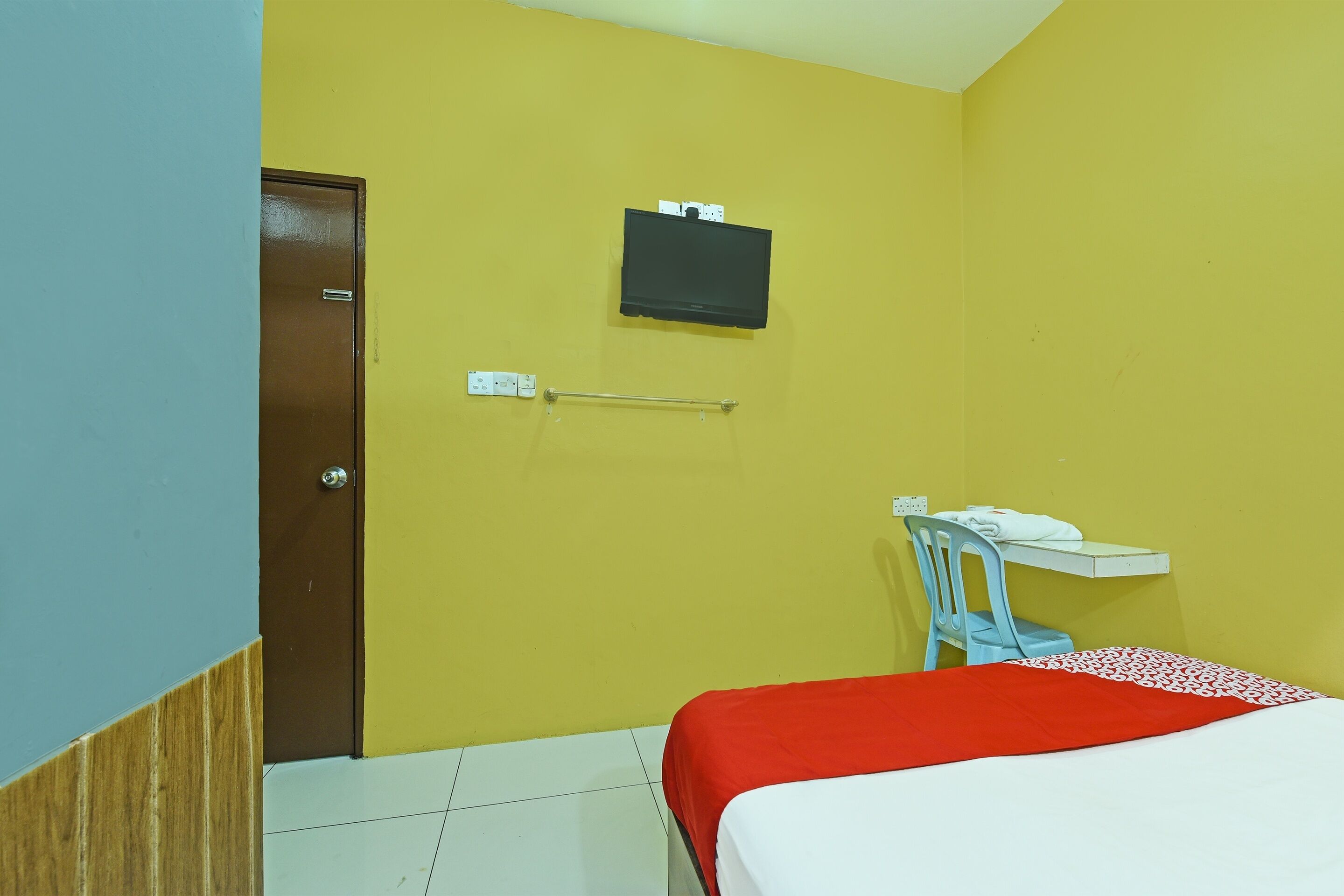 Una habitación con cama, escritorio, silla, televisor montado en la pared y una puerta.