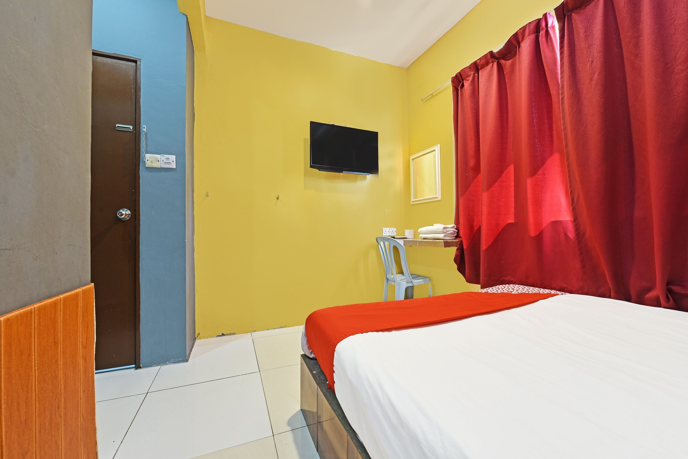 Una habitación de hotel con una cama, televisor, escritorio con silla y cortina roja.