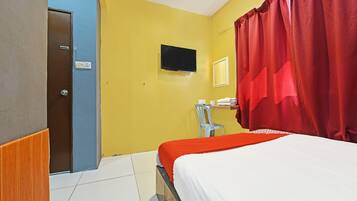 A hotel room with a bed, a television, a desk with a chair, and a red curtain.