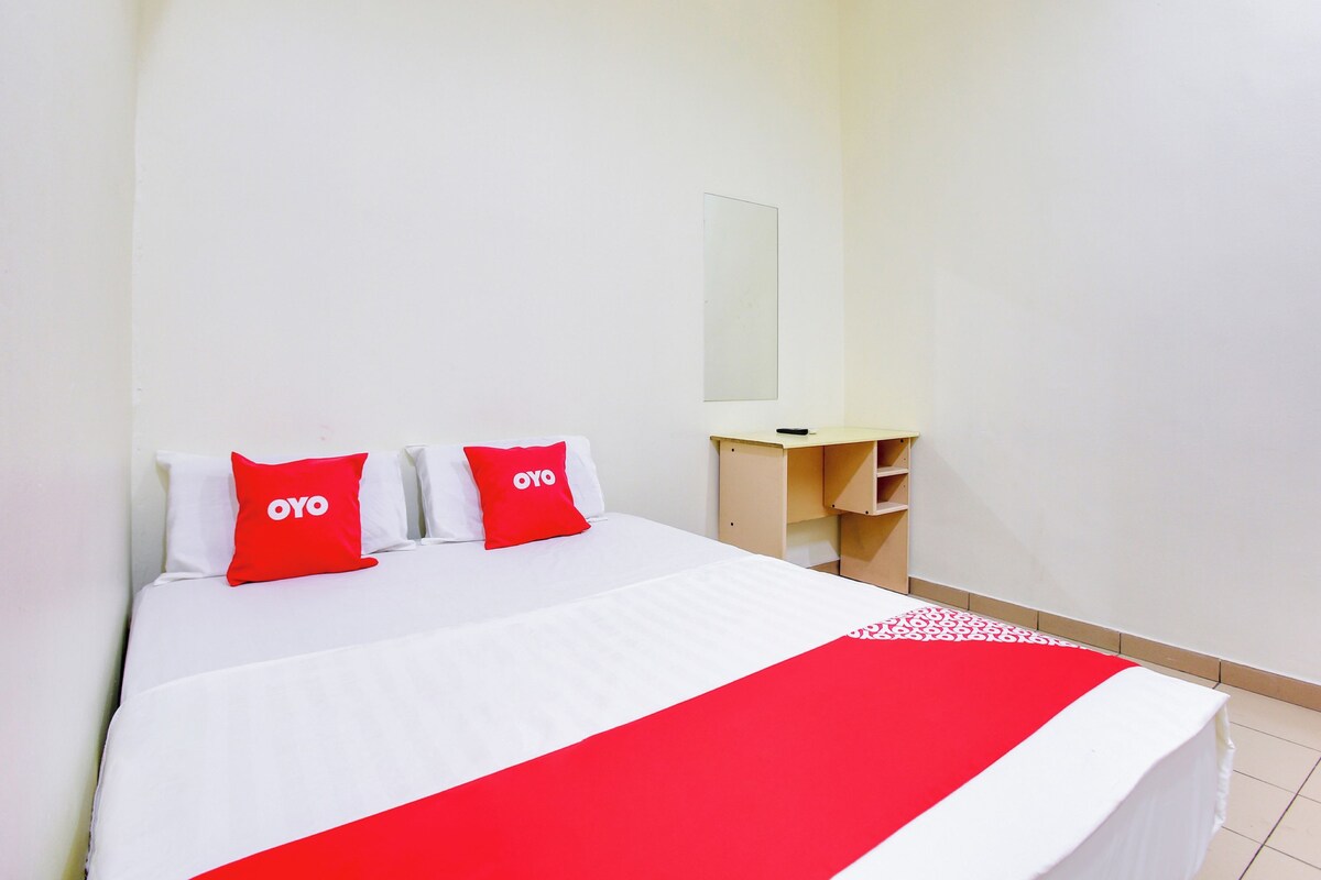 Habitación de hotel con cama, dos almohadas rojas con la marca 'OYO', una mesita de noche, un espejo y un corredor de cama rojo y blanco.