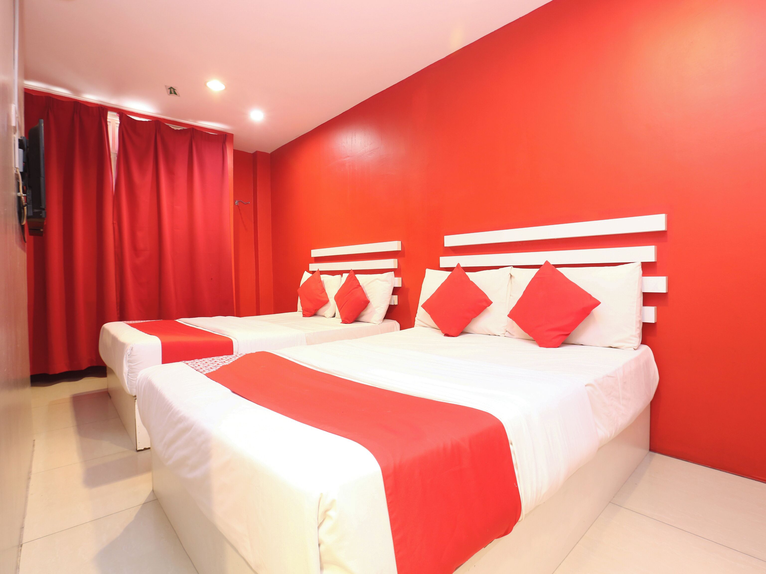 A hotel room with two beds, red curtains, and a red wall.