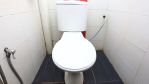 Une petite salle de bain aux dimensions réduites, avec des toilettes blanches, une tuyauterie visible et une cloison rouge.