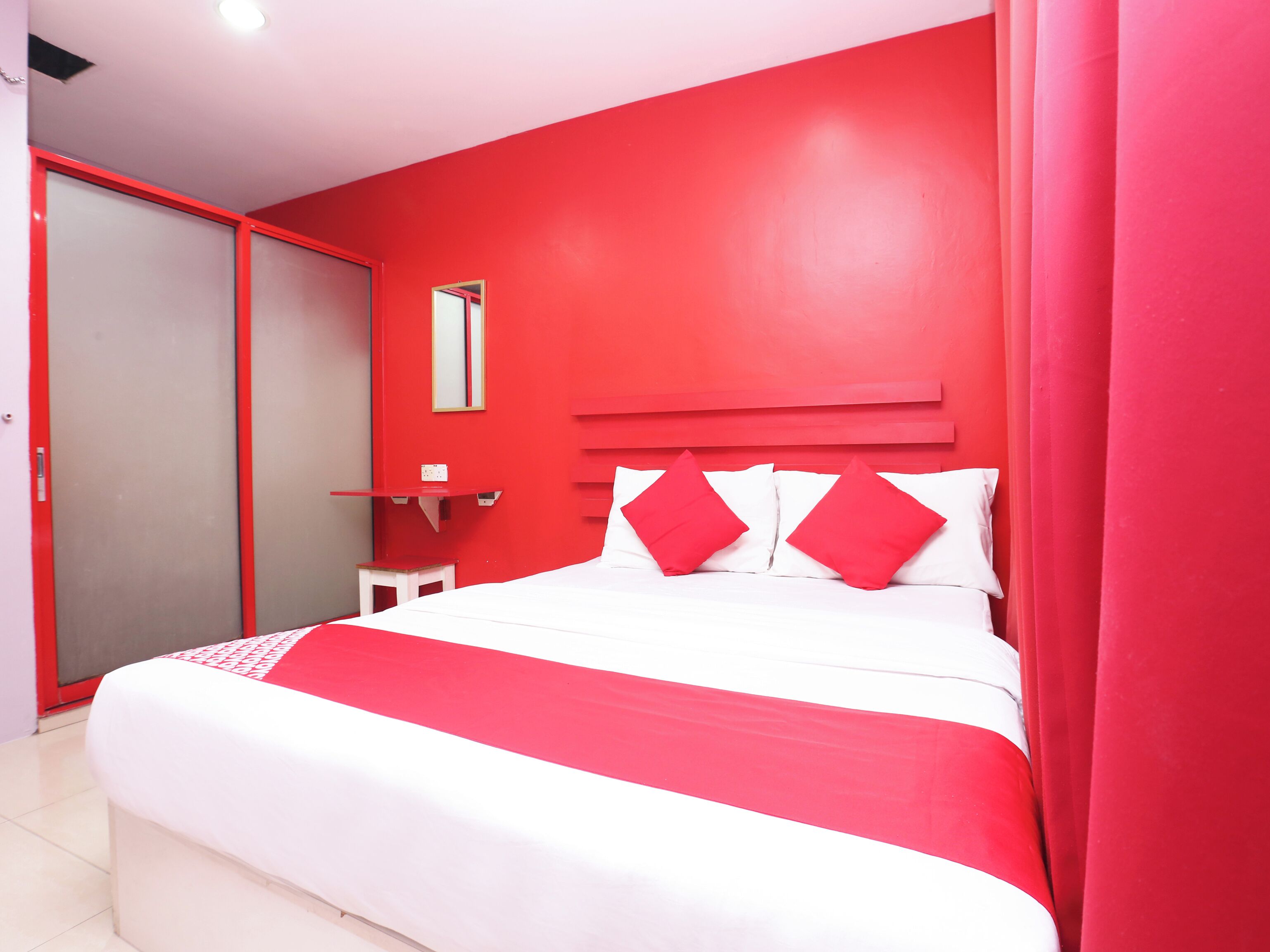 A room with a bed, a red wall, a white headboard, and a red curtain.