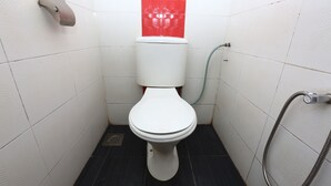Une petite salle de bain aux dimensions réduites, avec des toilettes blanches, un mur rouge et un flexible de douche.
