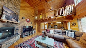 A cozy cabin interior with a stone fireplace, a large television, a sofa, and a dining area. - Acorn Acres is a true log cabin nestled in complete privacy and seclusion on acr (Broken Bow)