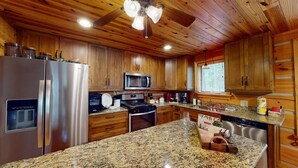 A kitchen with wooden cabinets, stainless steel appliances, granite countertops, and a ceiling fan. - Acorn Acres is a true log cabin nestled in complete privacy and seclusion on acr (Broken Bow)