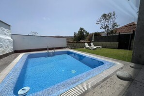 A rectangular swimming pool with a tiled edge, a ladder, and a lounge area with chairs. - Charming La Jara House with Private Pool and Stunning Mountain Views i (Arico)
