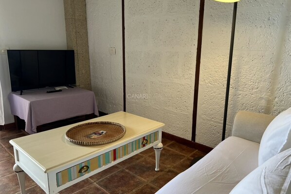 Une pièce avec un téléviseur posé sur un meuble, une petite table avec un plateau, un canapé blanc et un mur à texture.