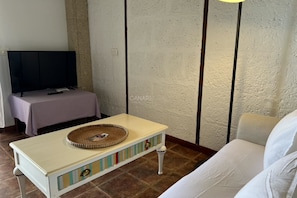 Una habitación con una televisión sobre un mueble bajo, una mesita con una bandeja, un sofá blanco y una pared con textura.