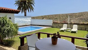 A pool area with a white wall, a palm tree, and a view of the hills. - Charming La Jara House with Private Pool and Stunning Mountain Views i (Arico)
