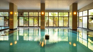 Une piscine intérieure avec des parois en verre transparent, de grandes fenêtres et un pilier central.