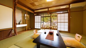 Une pièce de style japonais traditionnel, avec un sol recouvert de tatamis, une petite table avec un set de table, des coussins et une porte coulissante donnant sur l’extérieur.