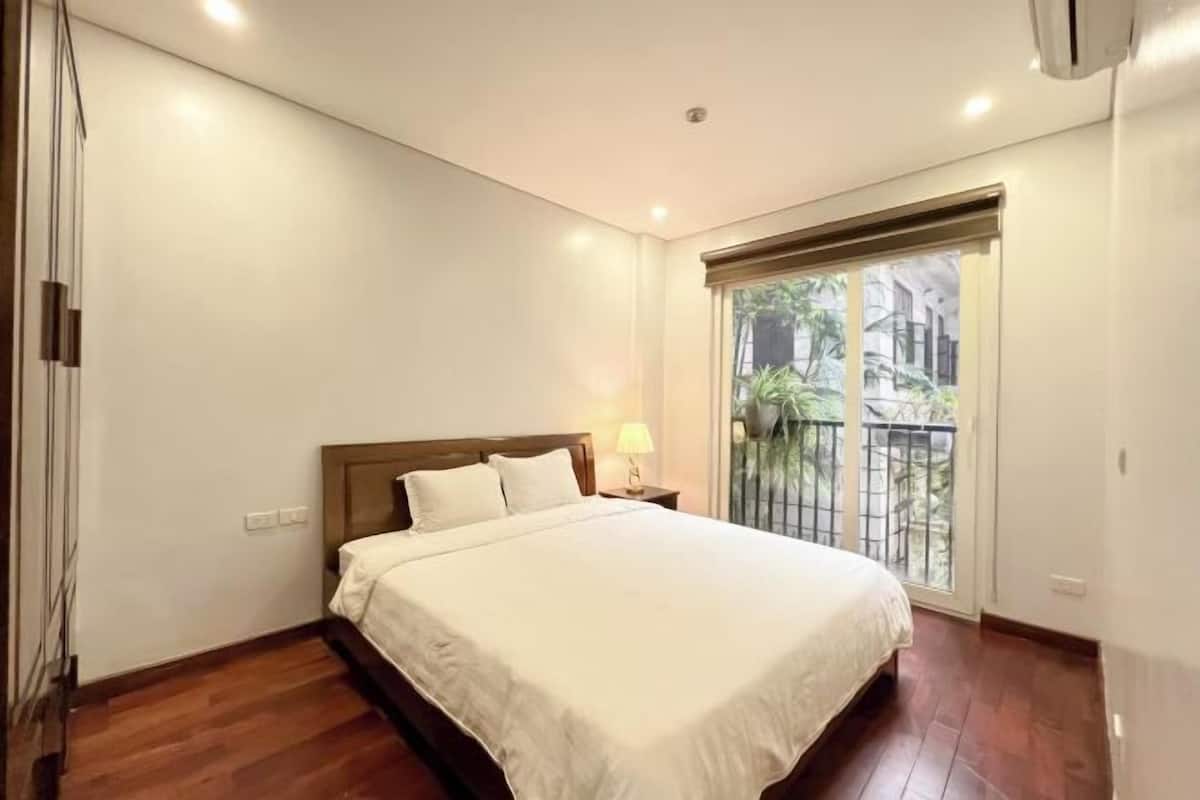 A bedroom with a bed, a nightstand, a window with a view, and a door.
