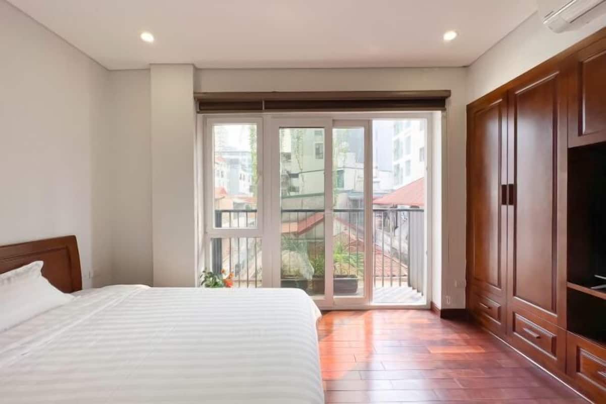 A bedroom with a large bed, a sliding glass door to a balcony, and wooden furniture.