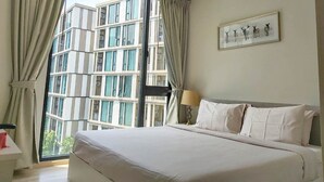 Quarto de hotel com uma cama grande, mesa de cabeceira, luminária e janela com cortinas.