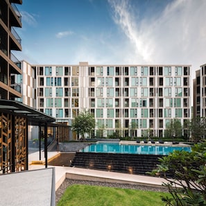 Un moderno edificio de varios pisos con piscina, mobiliario exterior y un jardín bien cuidado.