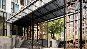 Um edifício moderno com entrada coberta, escadaria e vista para edifícios vizinhos.