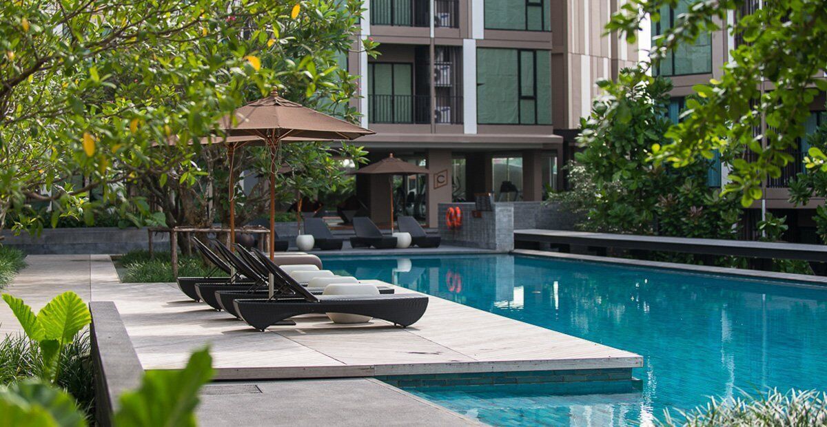 Piscina com espreguiçadeiras e guarda-sóis, cercada por vegetação e edifícios modernos.