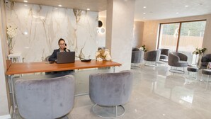 A modern reception area with a marble wall, a receptionist at a desk with a laptop, and grey upholstered chairs. - Spa Hotel Orbita (Blagoevgrad)