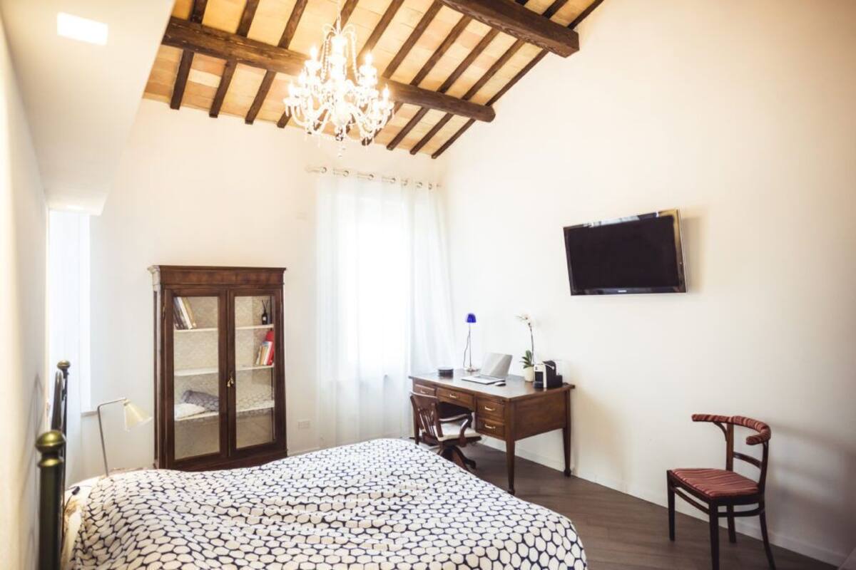 Un dormitorio con una cama, un armario de madera, un escritorio con una silla, un televisor y una araña.