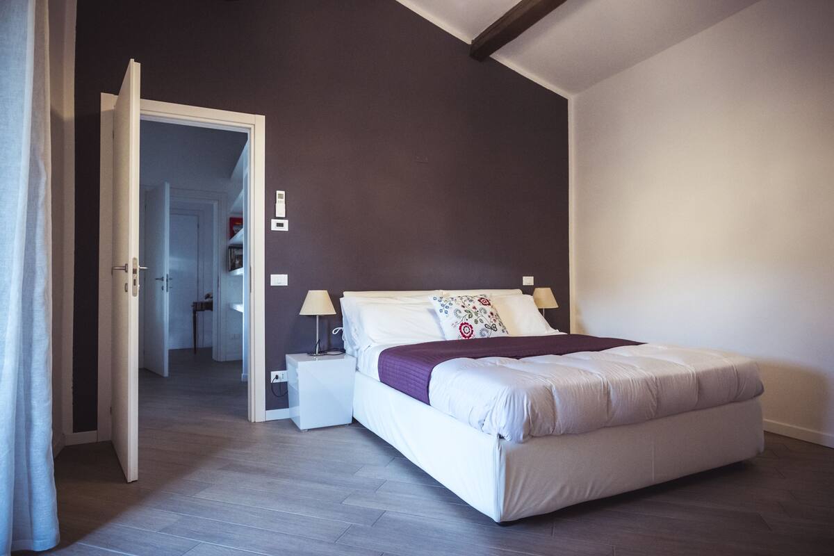 Un dormitorio con cama, mesitas de noche y una puerta que da a otra habitación.