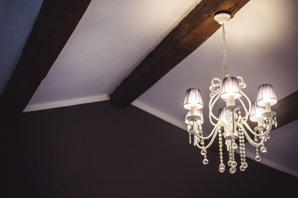 A chandelier with multiple lights hanging from a ceiling with exposed wooden beams.