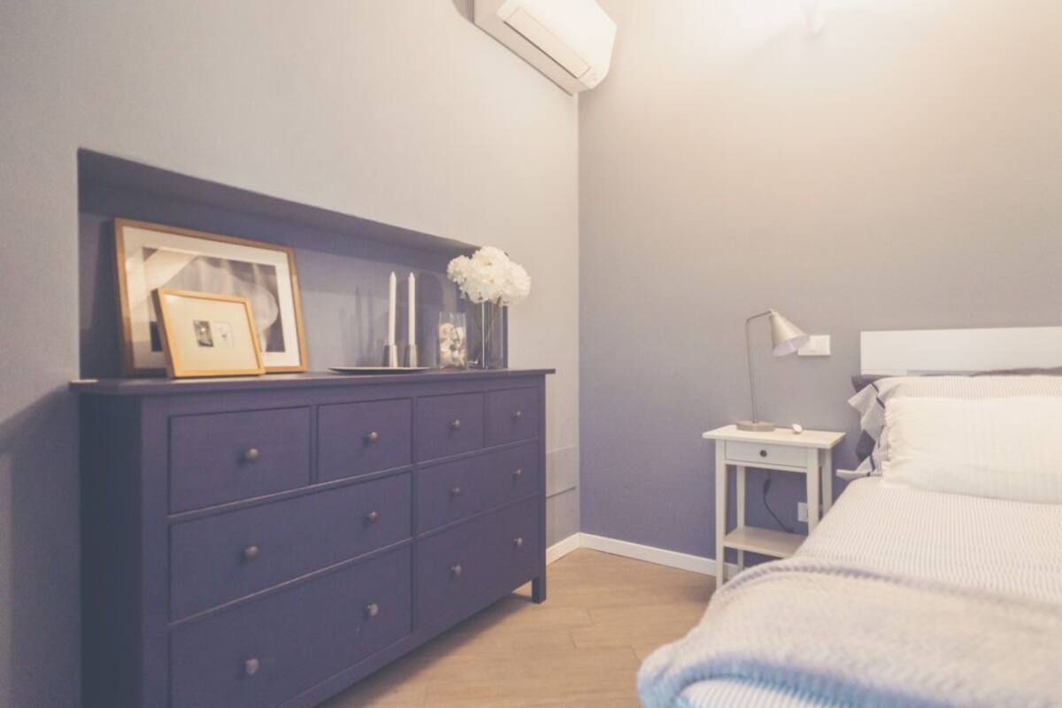 Un dormitorio con una cama, un tocador, una mesita de noche y un aire acondicionado instalado en la pared.