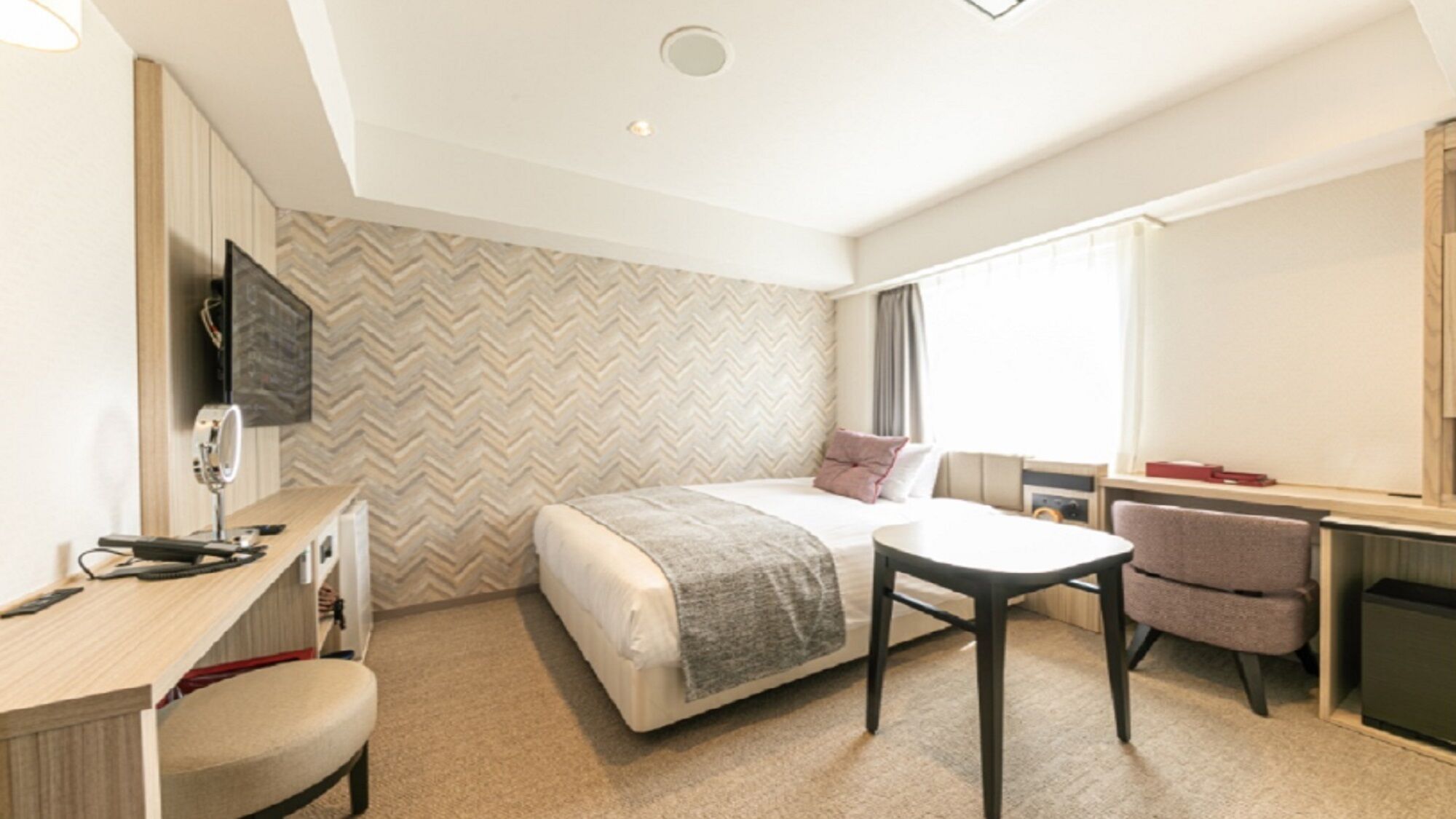 Una habitación de hotel con cama, escritorio, silla y televisor montado en la pared.