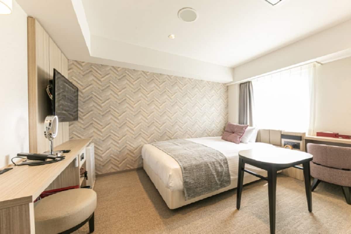 A hotel room with a bed, desk, chair, and a television mounted on the wall.