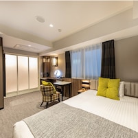 A hotel room with a bed, a desk, a chair, a mirror, and a window with curtains.