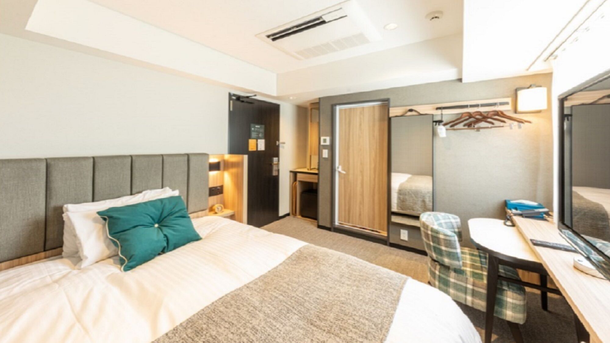 Habitación de hotel con cama, mesita de noche, espejo, armario y escritorio con silla.
