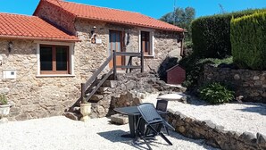 Un bâtiment en pierre avec un toit recouvert de tuiles rouges, une porte en bois et une fenêtre dotée d’un cadre en bois.