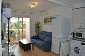 Enjoy a compact living space with a sofa, dining table, and kitchenette featuring a refrigerator, microwave, and washing machine.