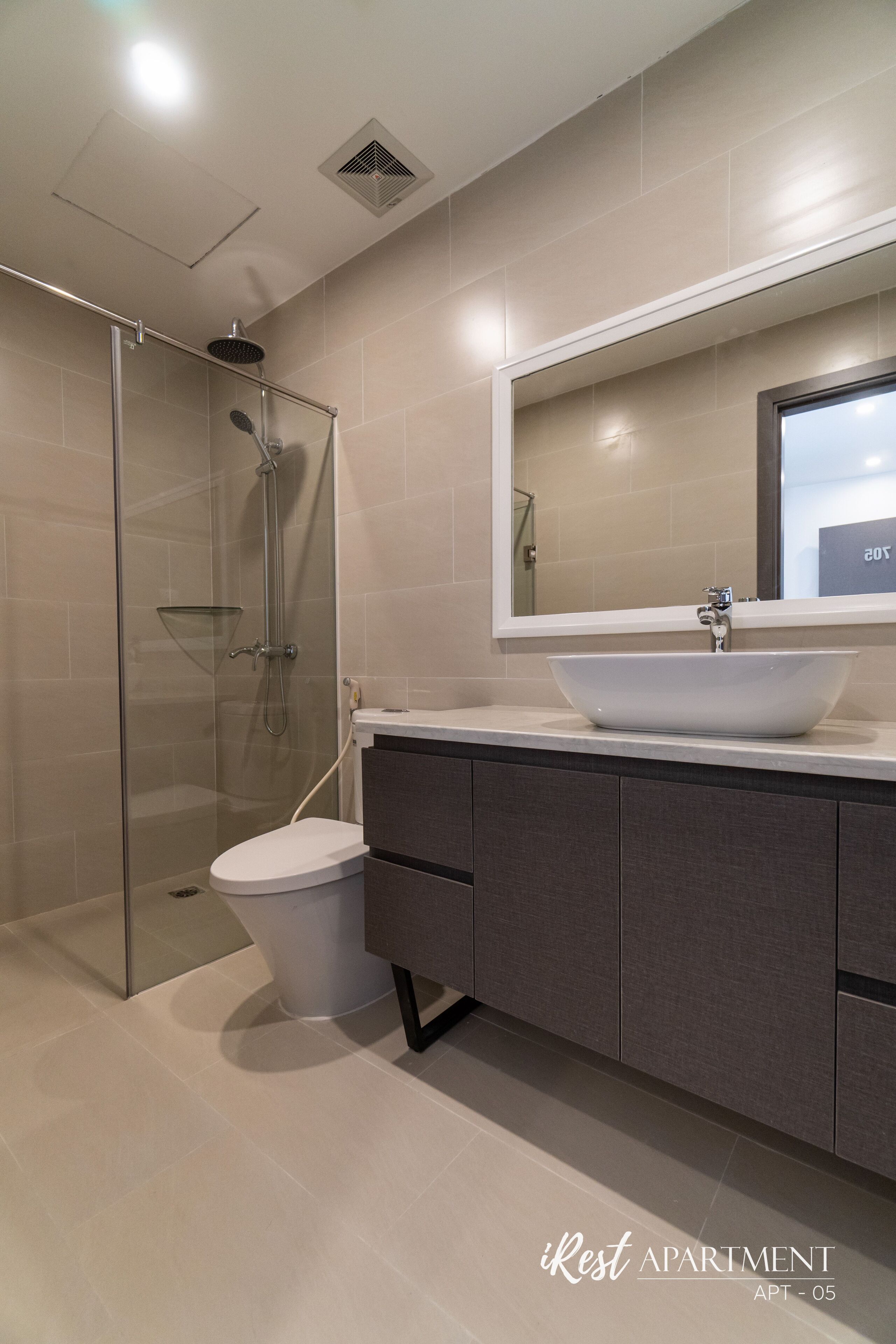 Un baño moderno con ducha de vidrio, un lavabo blanco con recipiente y un espejo grande sobre el mueble.